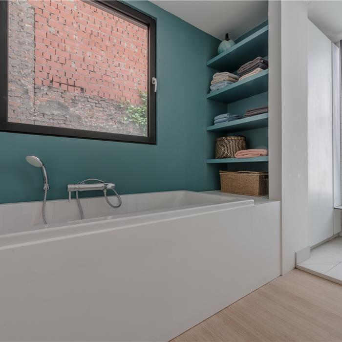 Bad met groenblauwe accentwand en open wandplanken in badkamer in Antwerpen