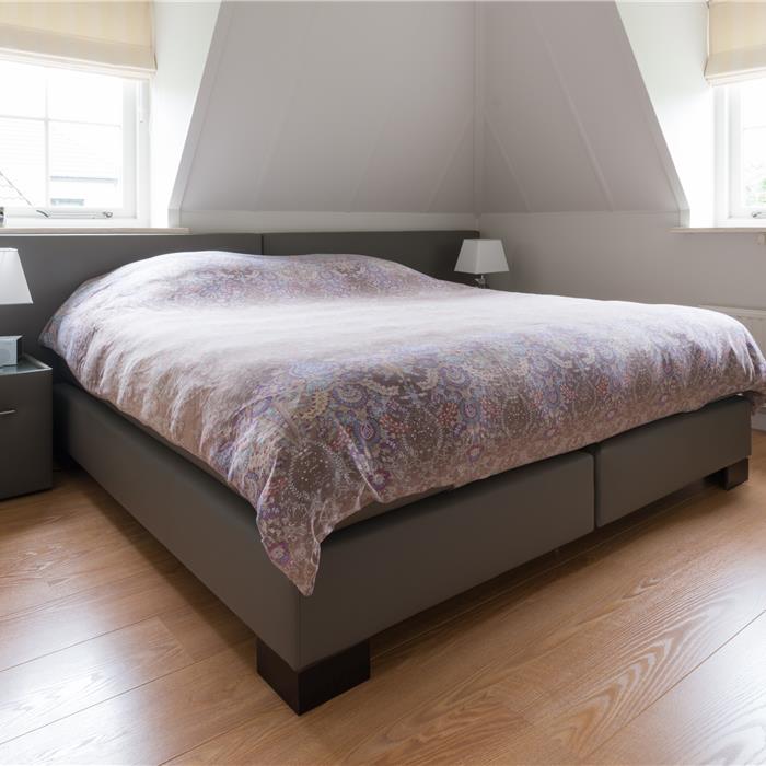 Grijze boxspring met op maat ingekort hoofdbord tussen twee dakramen