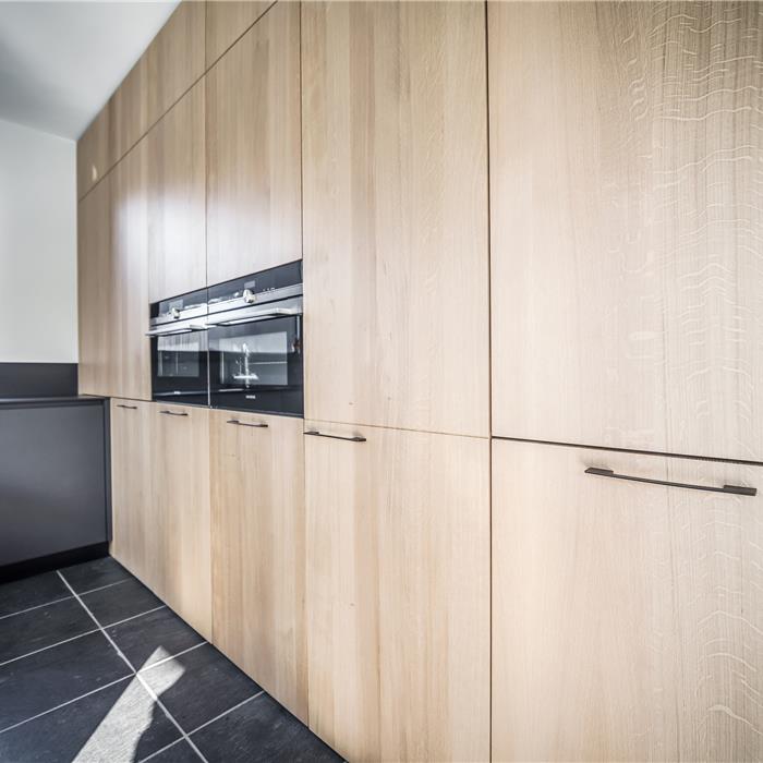 Detail van hoge houten keukenkasten op maat met geïntegreerde zwarte ovens
