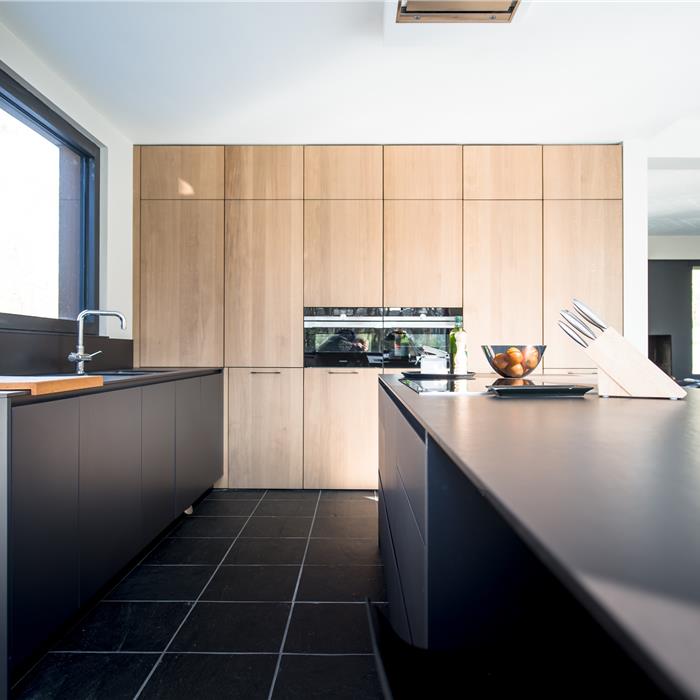 Hoge keukenkastenwand in licht hout met geïntegreerde ovens en zwart kookeiland