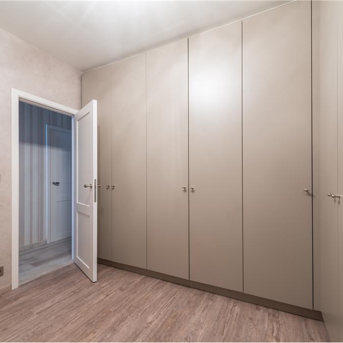 Dressing met maatkasten in hoekopstelling en hoge crèmekleurige deuren