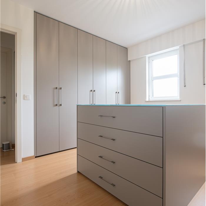 Dressing in Essen met kamerhoge taupekleurige maatkasten en een centraal ladeblok met ruime laden.