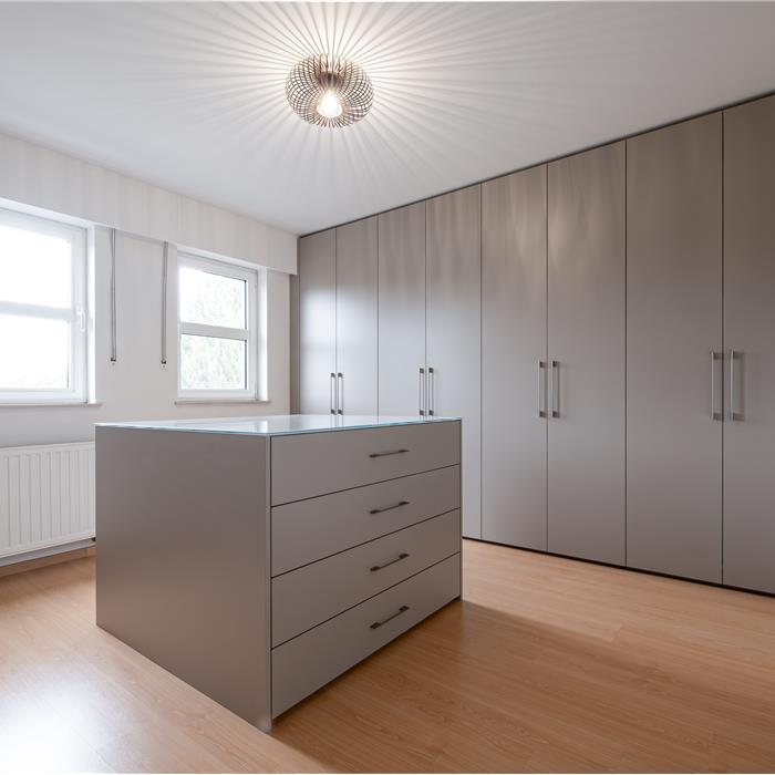 Overzicht van de dressing in Essen met kamerhoge taupekleurige maatkasten en een centraal ladeblok.