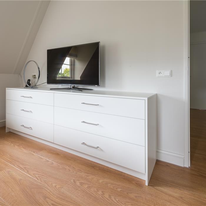 Witte commode op maat met televisie onder schuin dak in slaapkamer