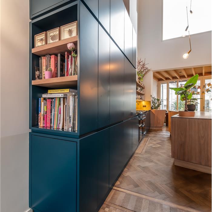 Blauwe maatkeuken in Antwerpen met hoge maatkasten, open houten vakken en houten kookeiland