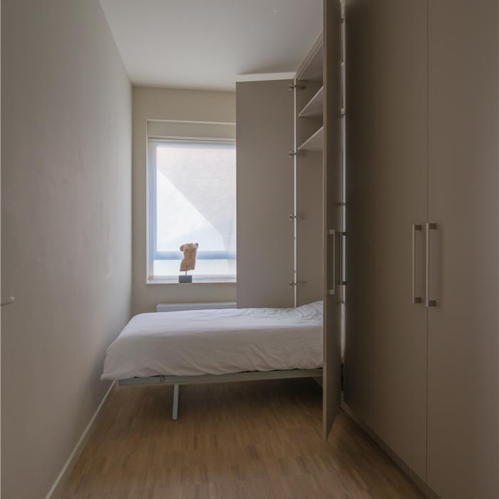 Uitgeklapt bed uit kamerhoge kastenwand in smalle logeerkamer