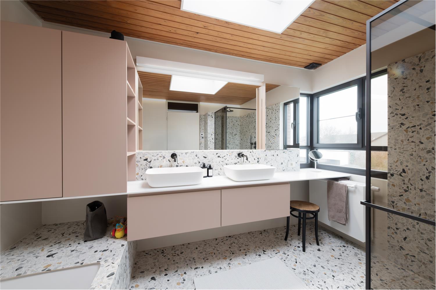 Overzicht van het antiekroze badkamermeubel met wit solid-surfacewerkblad en terrazzo in Vorselaar.