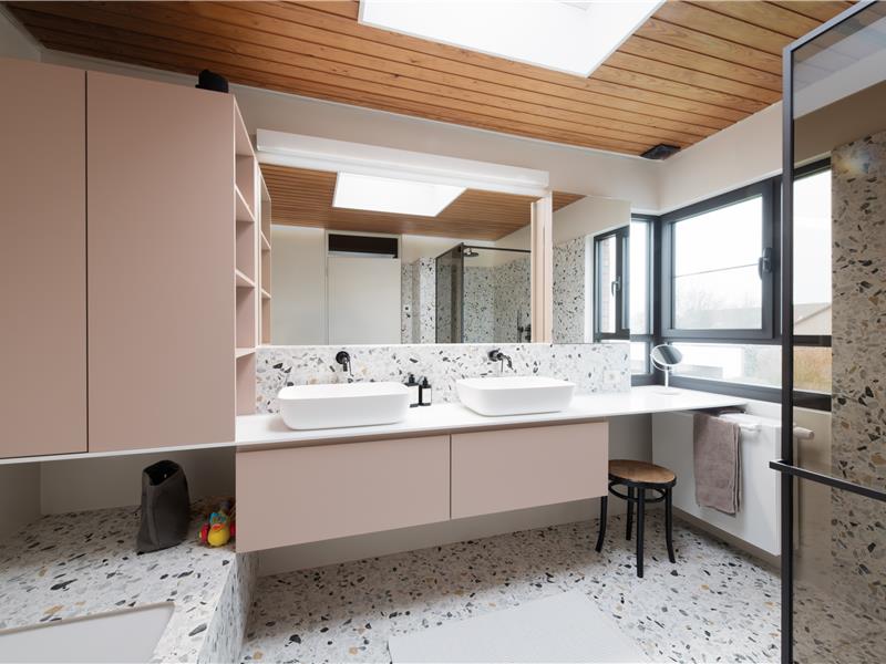 Overzicht van het antiekroze badkamermeubel met wit solid-surfacewerkblad en terrazzo in Vorselaar.